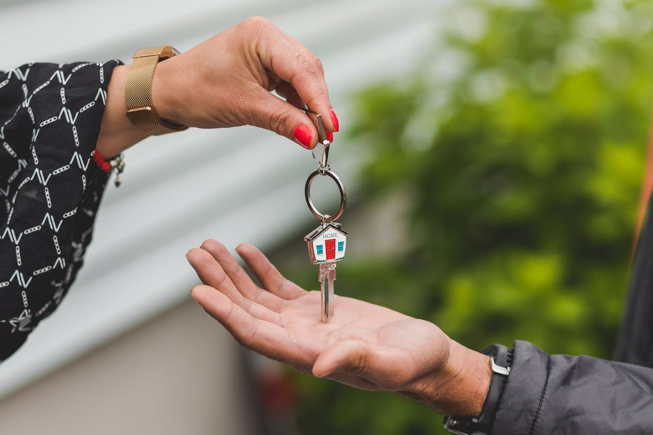 services-07 Close-up of a hand handing over a key with a house keychain, symbolizing real estate transaction.